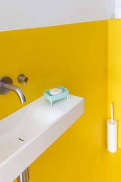 Držač i ribež za sapune bubble buddy stoji na modernom bijelom umivaoniku u kupaoni sa žutim zidom