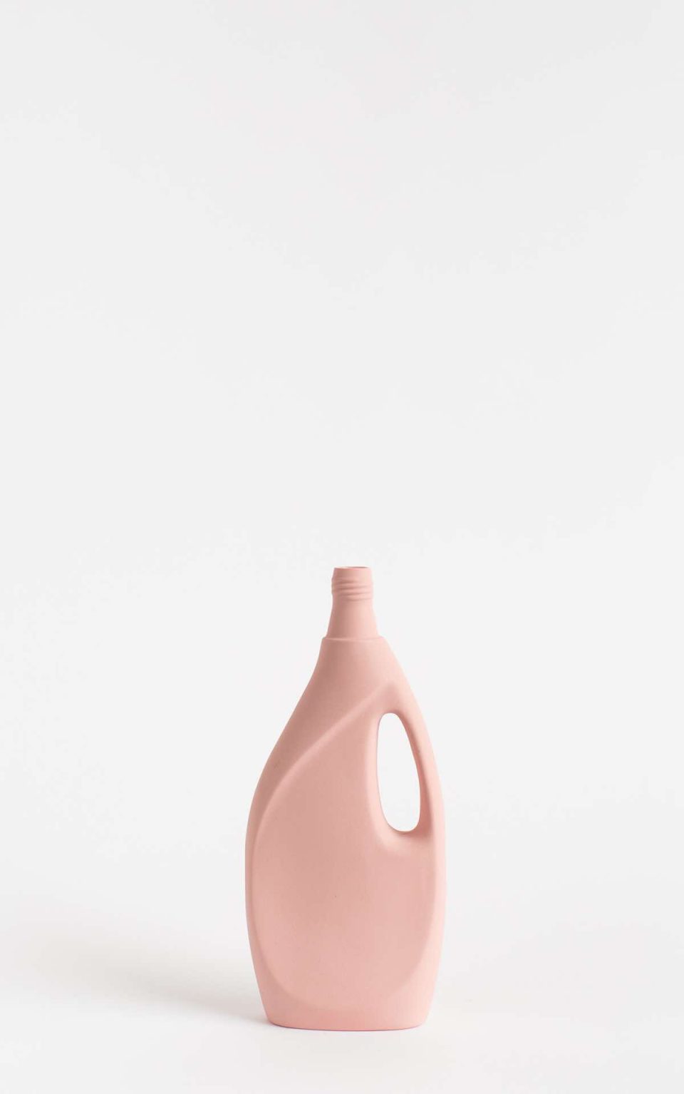 Prikazana je vaza brenda foekje fleur u svijetlo ružićastoj boji ispred sive pozadine. Vaza ima oblik kontejnera za sredstvo za pranje suđa.