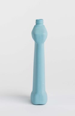 Prikazana je vaza brenda foekje fleur u svijetlo plavoj boji ispred sive pozadine. Vaza je prikazana s bočne strane, ima oblik kontejnera za sredstvo za pranje suđa.