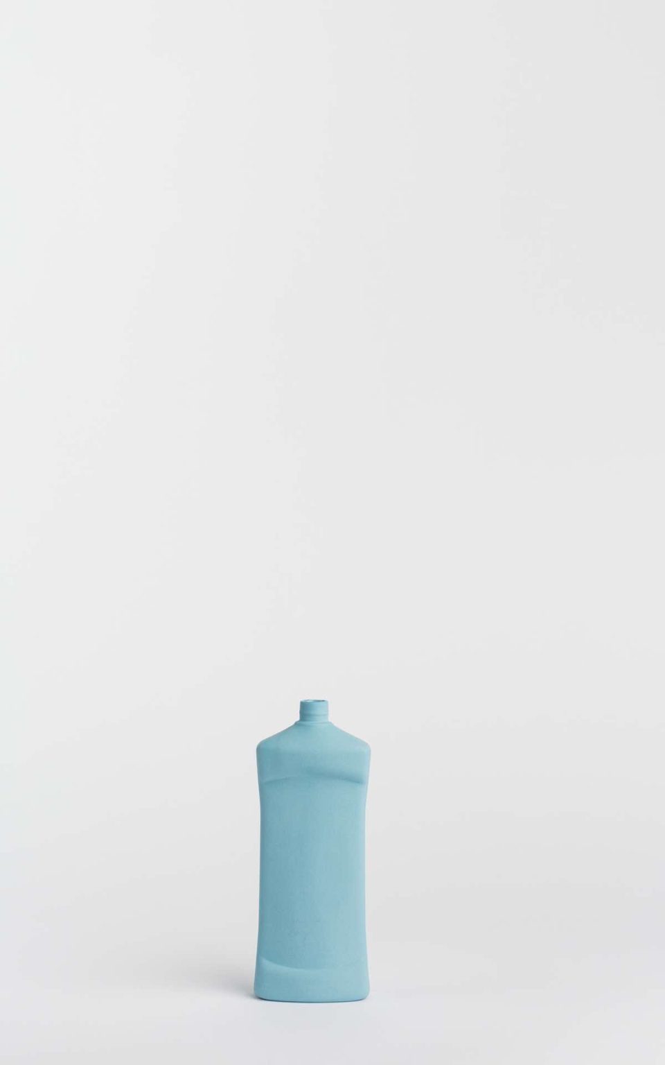 Prikazana je vaza brenda foekje fleur u svijetlo plavoj boji ispred sive pozadine. Vaza ima oblik kontejnera za sredstvo za pranje suđa.