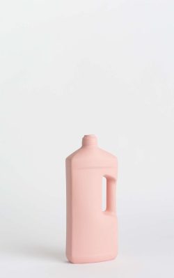 Prikazana je vaza brenda foekje fleur u svijetlo ružićastoj boji ispred sive pozadine. Vaza ima oblik kontejnera za sredstvo za pranje suđa. Vaza je prikazana lagano zaokrenuto na bočnu stranu.