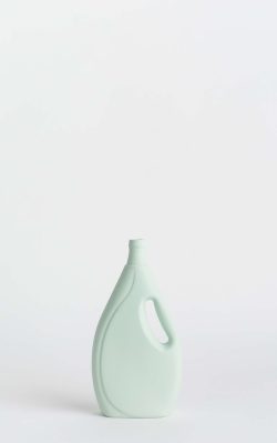 Prikazana je vaza brenda foekje fleur u svijetlo zelenoj boji ispred sive pozadine. Vaza ima oblik kontejnera za sredstvo za pranje suđa.