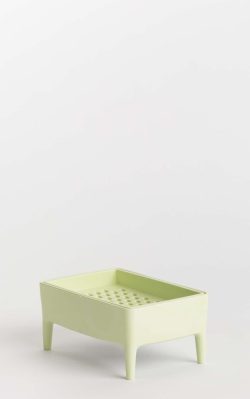 Slika prikazuje proizvod bubble buddy, držač i ribež za sapun u jednom. Plastična kutija je pistachio boje, s malim nogicama i ribežom na poklopcu. Pozadina je sive boje.