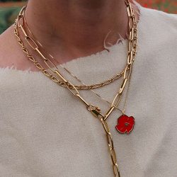 Žena u bijeloj bluzi, s vrata vise nekoliko zlatnih lančića, jedan pozlaćeni lančići s privjeskom u obliku crvenog cvijeta maka
