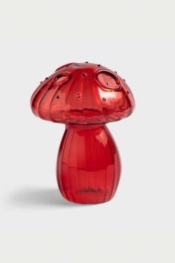 Na slici je staklena vaza u obliku gljive crvene boje. Vaza ima nekoliko rupica za cvjetiće na klobuku, stoji na sivoj pozadini