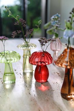 Naslici se vide male staklene vaze u obliku raznih gljiva u raznim bojama; u vaze su utaknuti razni cvjetići- Stoje na stolu od kamena, u pozadini se vidi interijer