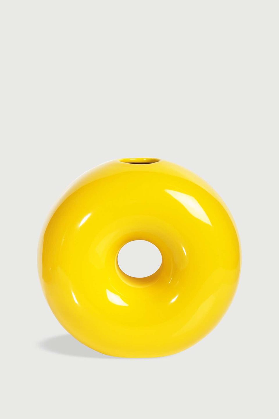 Na slici je prikazana keramičak vaza u obliku kruga s rupom u sredini. Vaza je žute boje i ima malu rupu na vrhu.