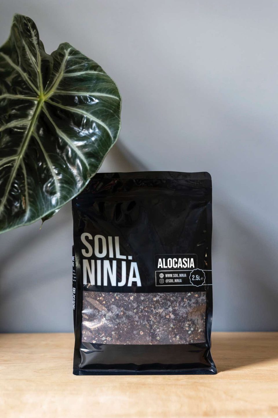 Na slici se vidi vreća supstrata od 2,5 kg proizvođača Soil.Ninja za alokasije. Uz vreću se na lijevoj strani vidi list alokasije 'Pink dragon'.